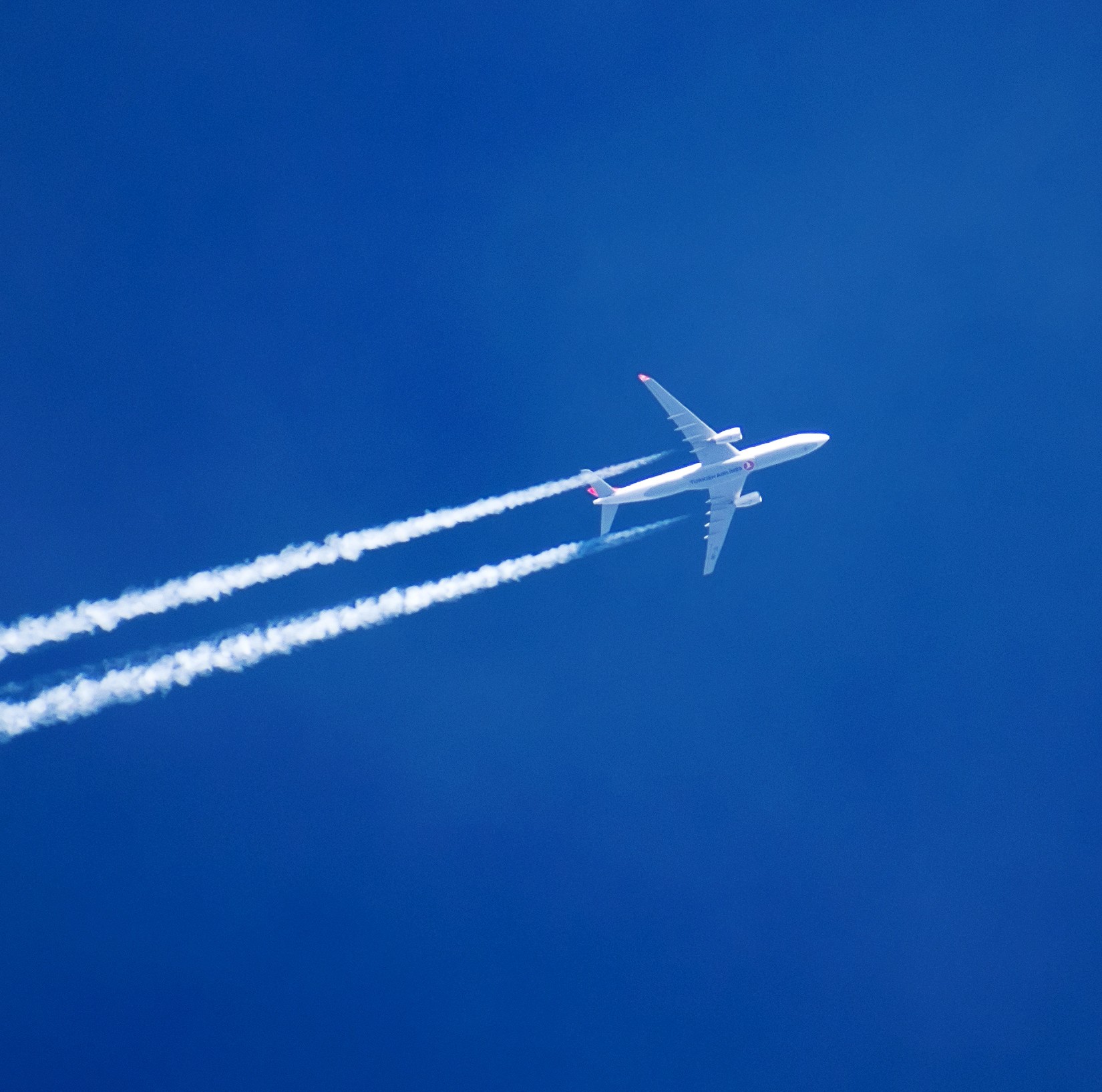 Bild eines Flugzeugs mit Kondensstreifen am blauen Himmel